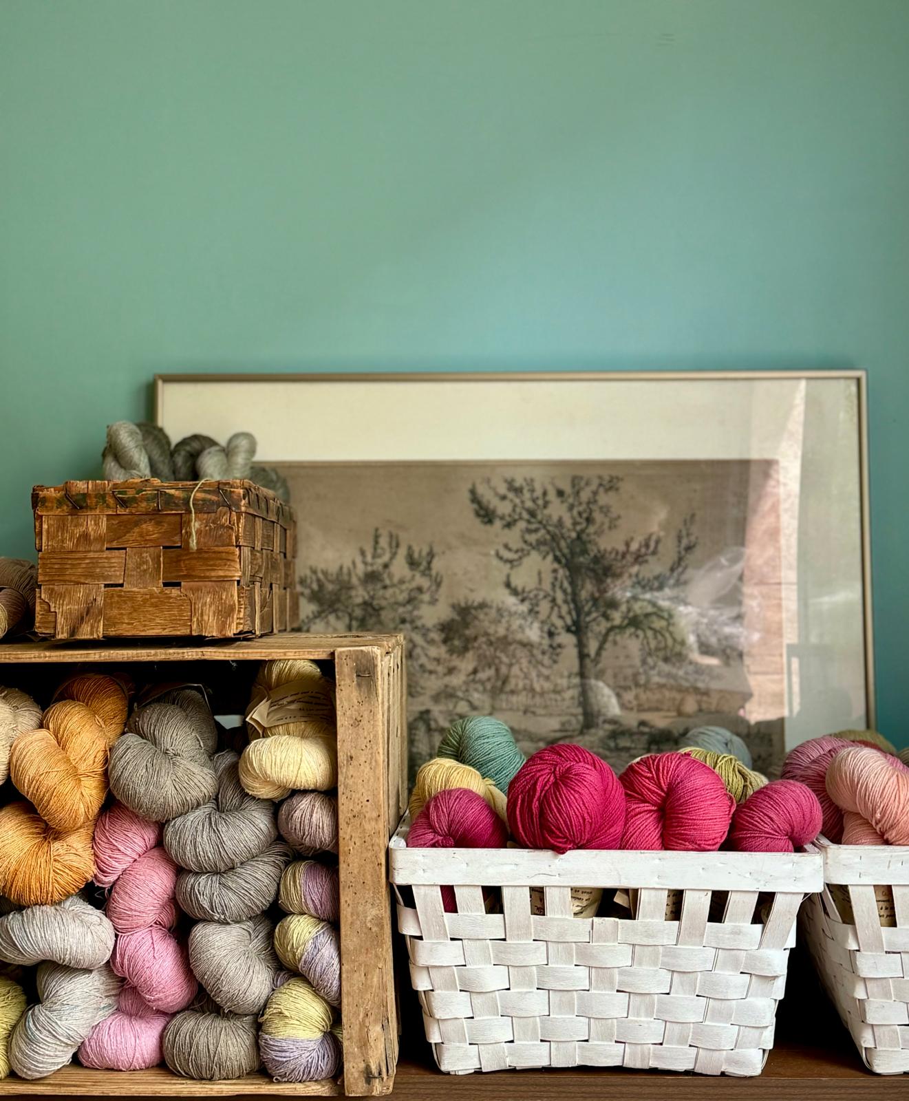 un coin de mon atelier, des fils colorés dans des caisses en bois vintage devant un tableau de moutons